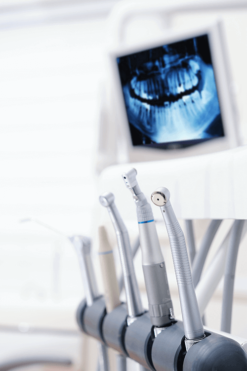 A close-up view of dental tools in a clinic, with a panoramic dental X-ray visible in the background.