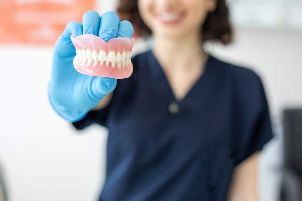 A dental professional wearing blue gloves holding a full set of removable dentures.