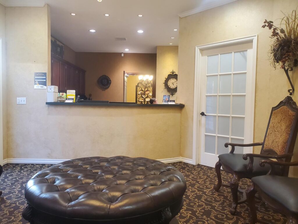 A warmly lit dental office reception area featuring a curved counter, decorative plants, and a framed mirror.